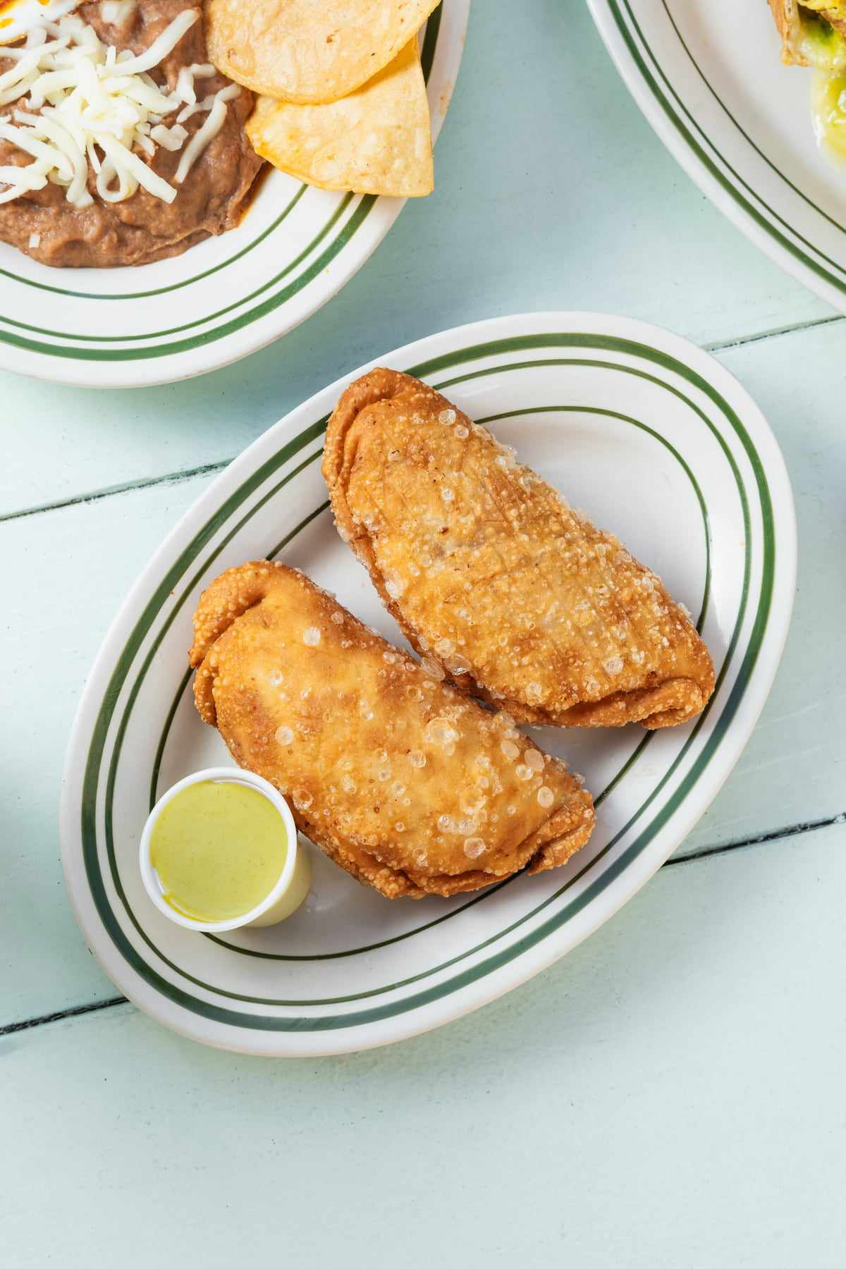 Two golden empanadas on a plate with a cup of green salsa