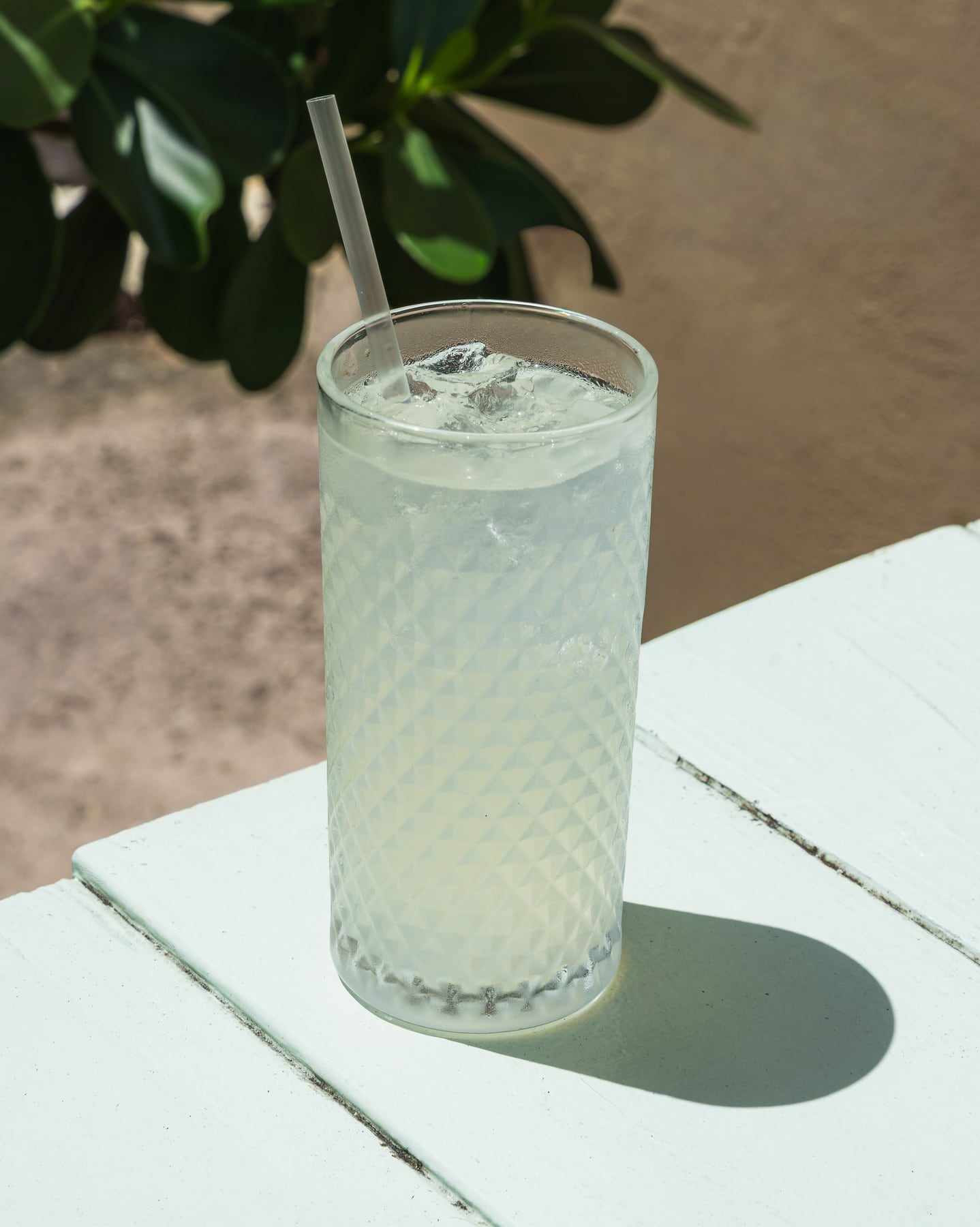 A tall glass of mint lemonade with ice on a pale blue table