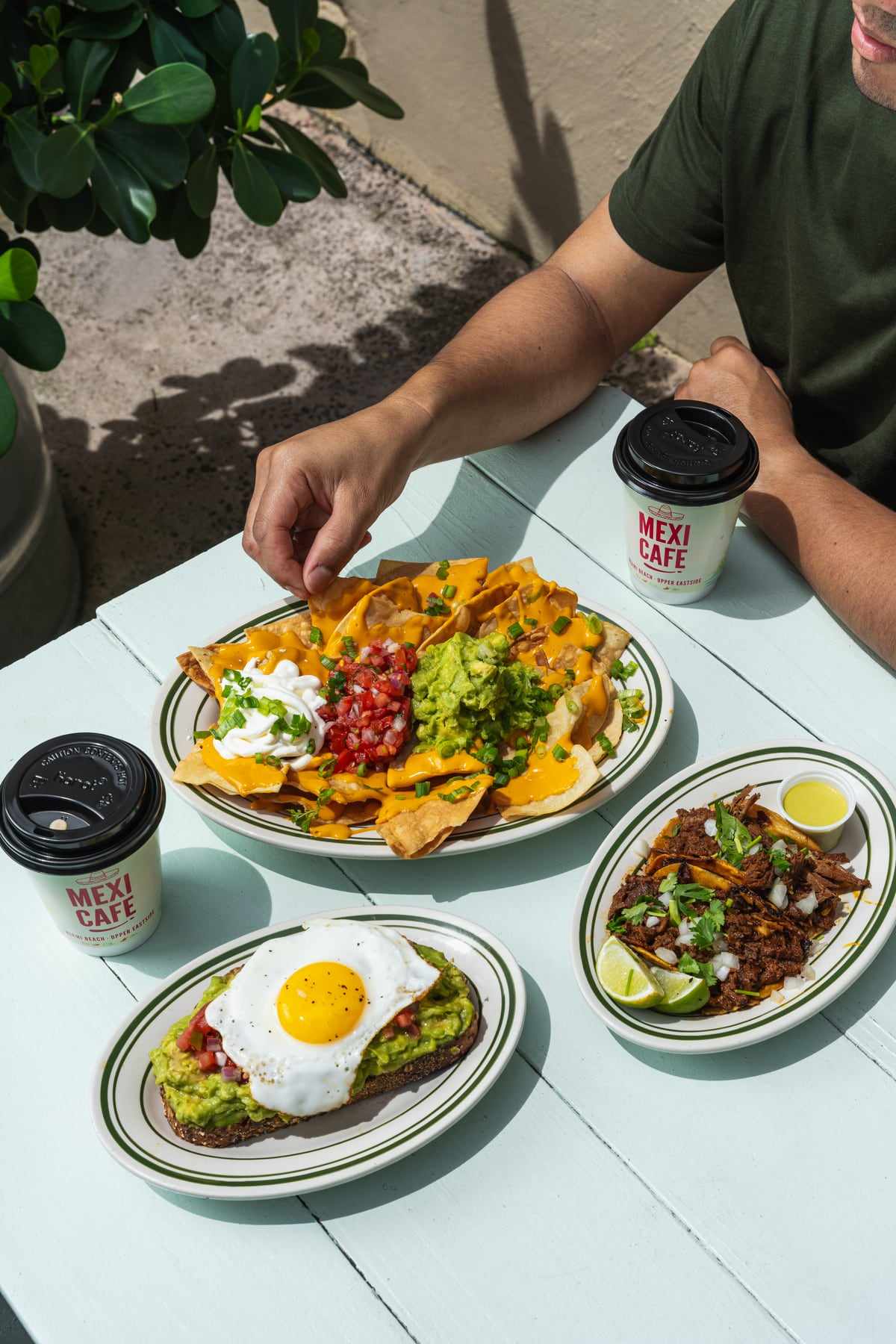 Loaded nachos, huevos rancheros and a Mexi Cafe coffee on a pale blue table outside the window